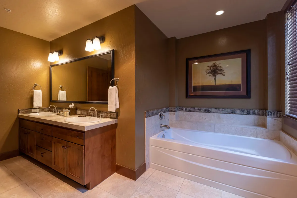 A serene, spa-inspired bathroom with a double sink vanity, large mirror, and a bathtub. Elegant touches like framed artwork elevate the soothing atmosphere, suggesting relaxation and renewal.
