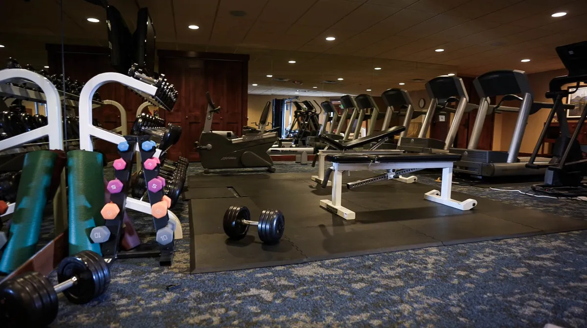 A modern, well-equipped fitness center featuring dumbbells, treadmills, and a weight bench, with guests actively working out and socializing. The space is energetic and designed for achieving fitness goals and group classes.