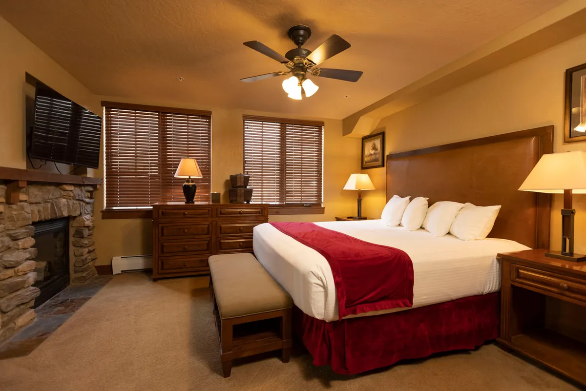 This interior photo features a spacious king bedroom complete with a plush king-sized bed, a wooden dresser, and a cozy fireplace. Sunlight streams through the window, creating a warm and restful ambiance. The room is designed for comfort and relaxation, perfect for unwinding after outdoor adventures.