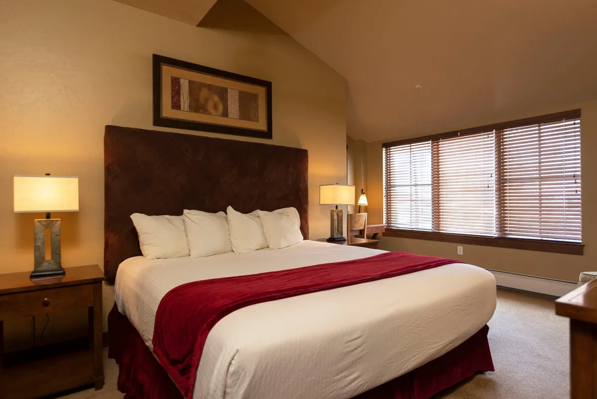 A queen bedroom styled with a bed featuring a red accent, decorative wall art, and table lamps. The mood is warm and inviting, offering an ideal space for adult guests or older children.