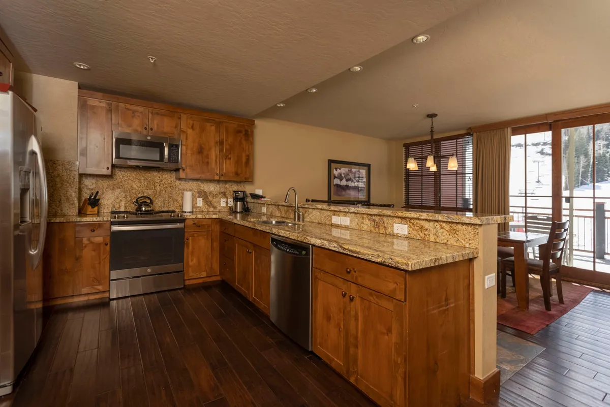 A combined kitchen and dining space with granite countertops, stylish stainless steel appliances, wood cabinetry, and large windows that illuminate the dining area. The open layout promotes easy flow between cooking, dining, and socializing—key for gatherings and planning adventures as mentioned in the section.