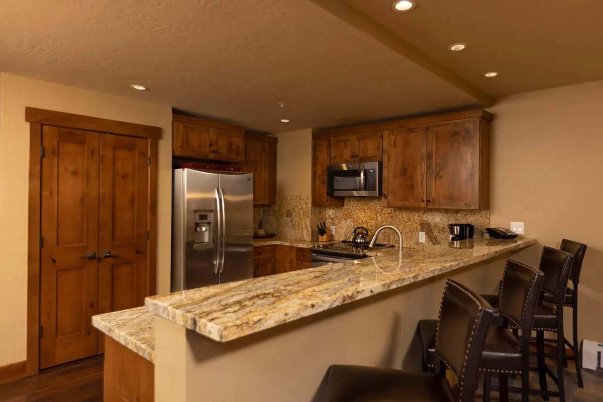 A welcoming kitchen scene showcasing granite countertops, stainless steel appliances, wood cabinetry, and bar stools tucked under the spacious island. The setting suggests a space for both meal prep and socializing, with plenty of room for guests or family to gather around the island.