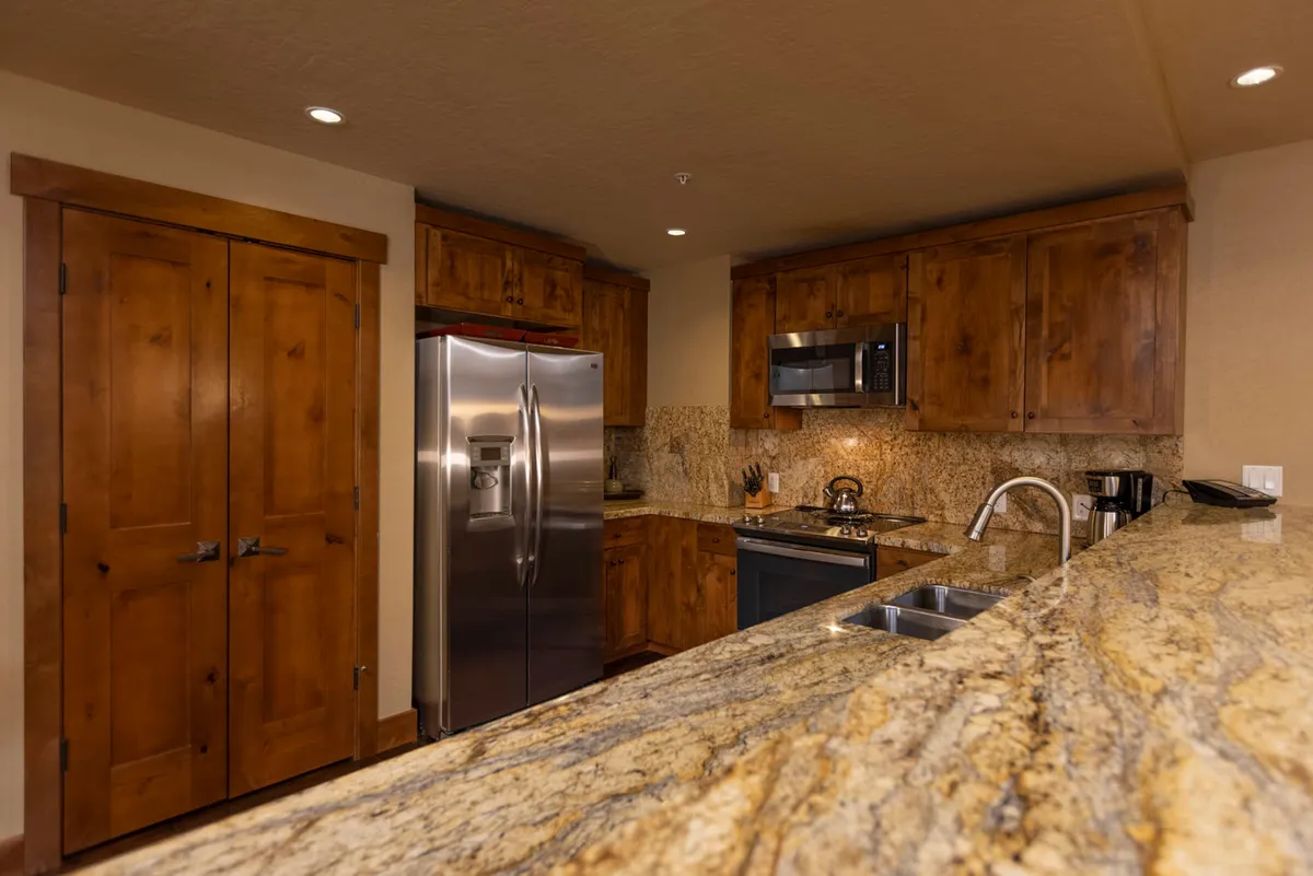 This image features a gourmet kitchen with granite countertops, gleaming stainless steel appliances, and warm wood cabinetry. The space is styled to evoke both functionality and comfort, ideal for preparing meals or entertaining guests. Details like a spacious countertop and open layout are visible, emphasizing culinary possibilities.